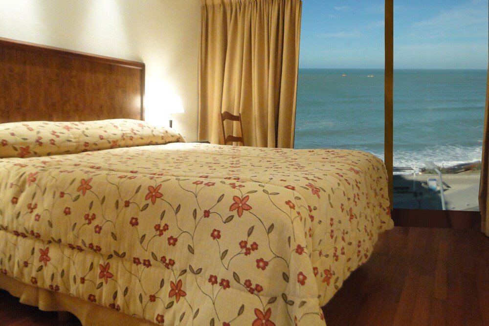 Dormitorio con cama, cabecera de madera, cortinas y vista al mar