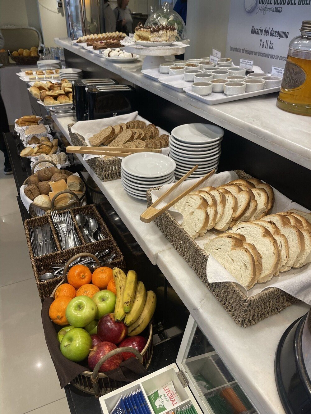 Buffet de desayuno con panes, facturas, frutas y condimentos