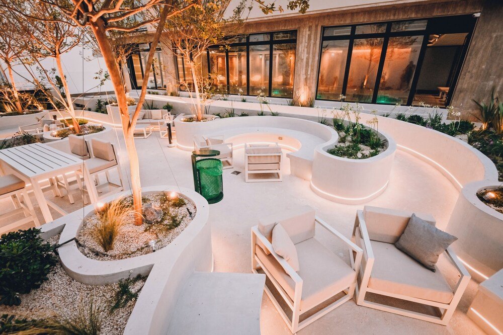Zona exterior con muebles blancos modernos rodeada de canteros y árboles