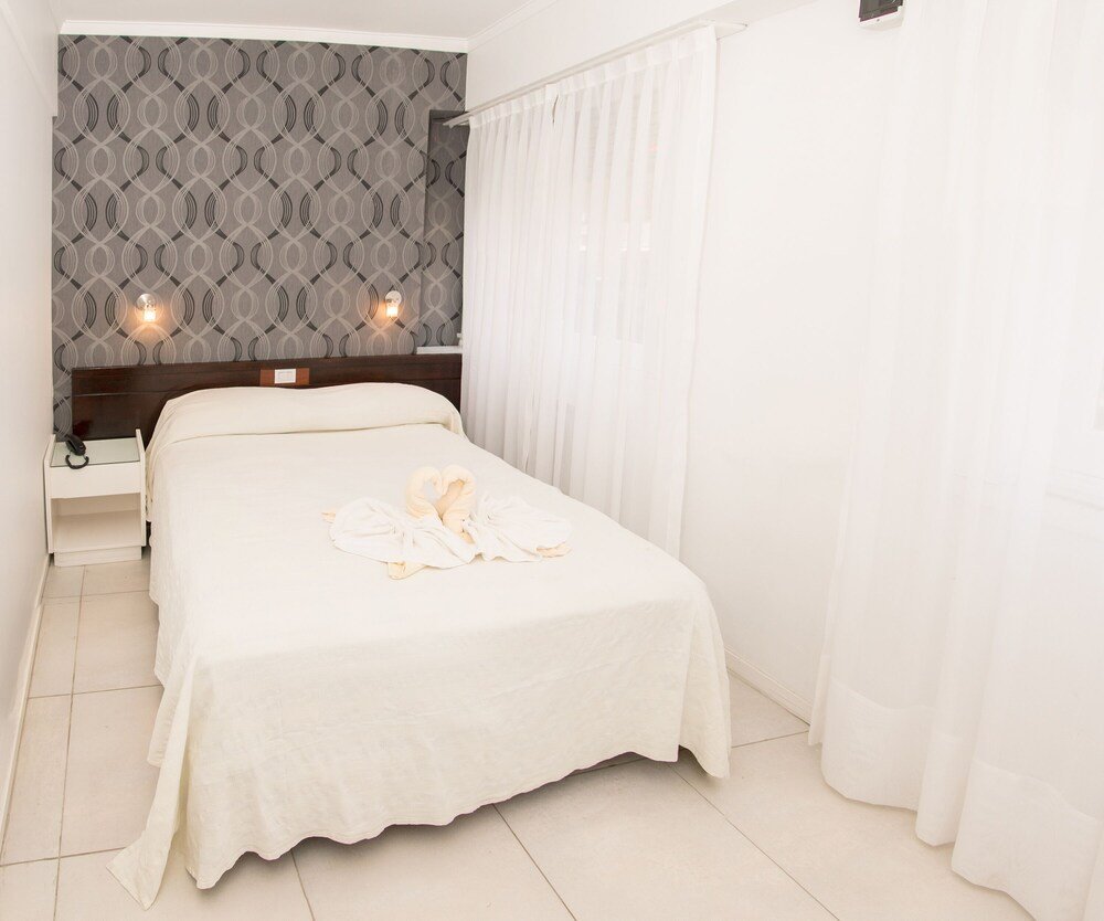 Cama con ropa blanca, mesa de luz con lámpara y empapelado