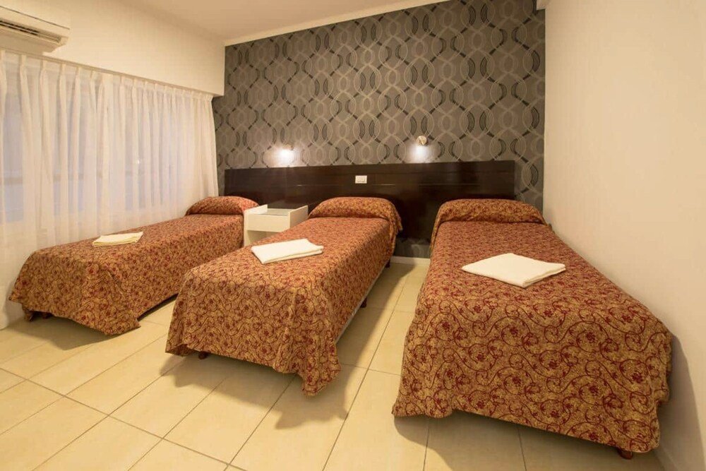 Habitación con tres camas individuales y ventanal con cortinas
