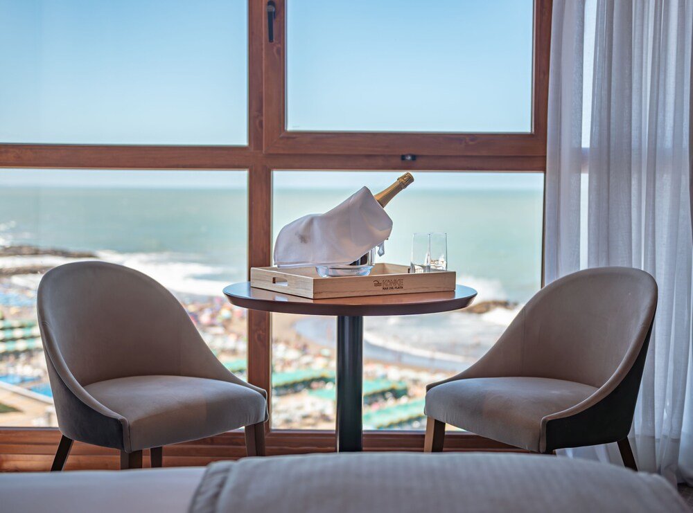 Habitación con gran ventana a la playa, mesa de madera, sillas y cama