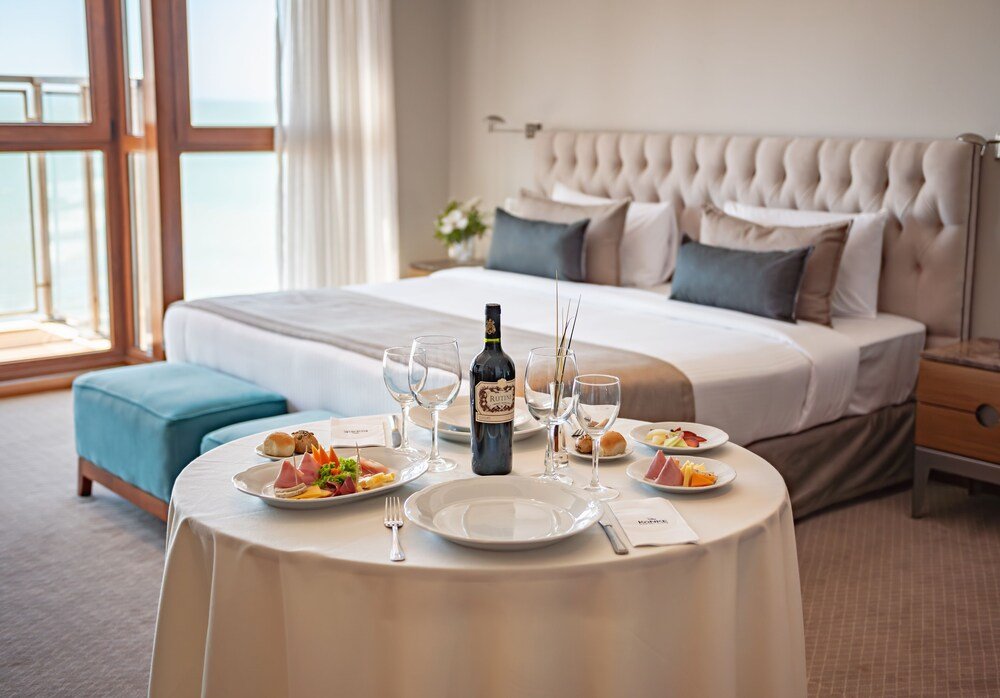 Mesa servida con platos, copas y vino en una habitación frente al mar