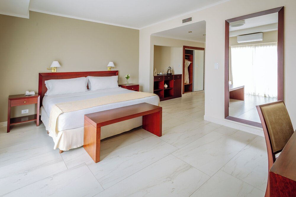 Habitación con cama, mesas de luz, banco y escritorio